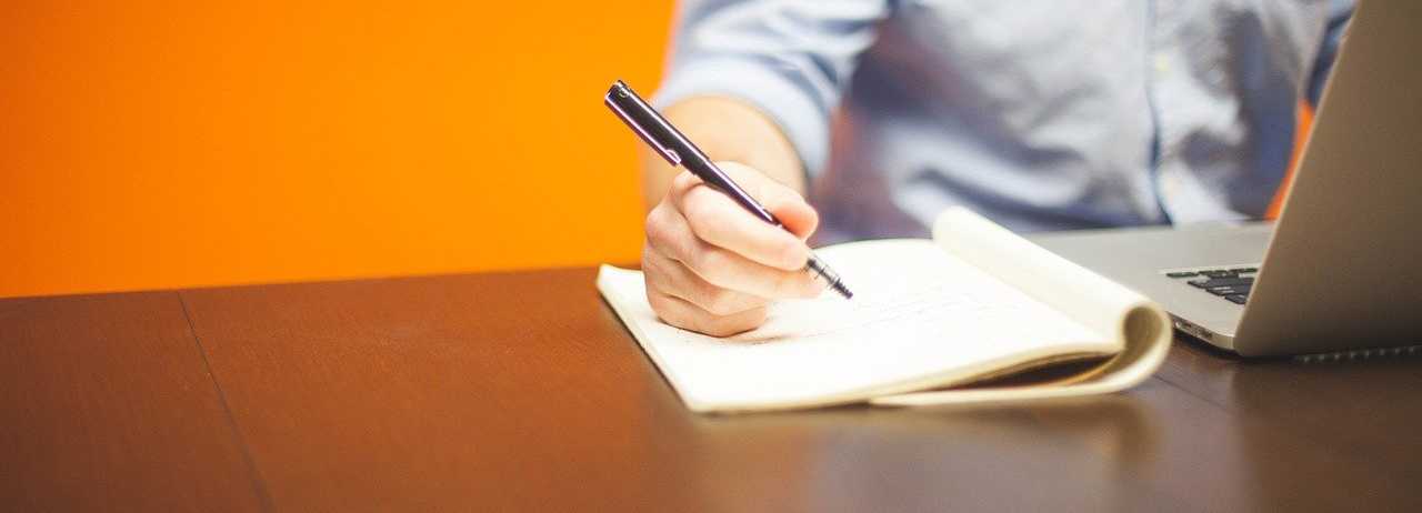 man writing on paper by computer horizontal